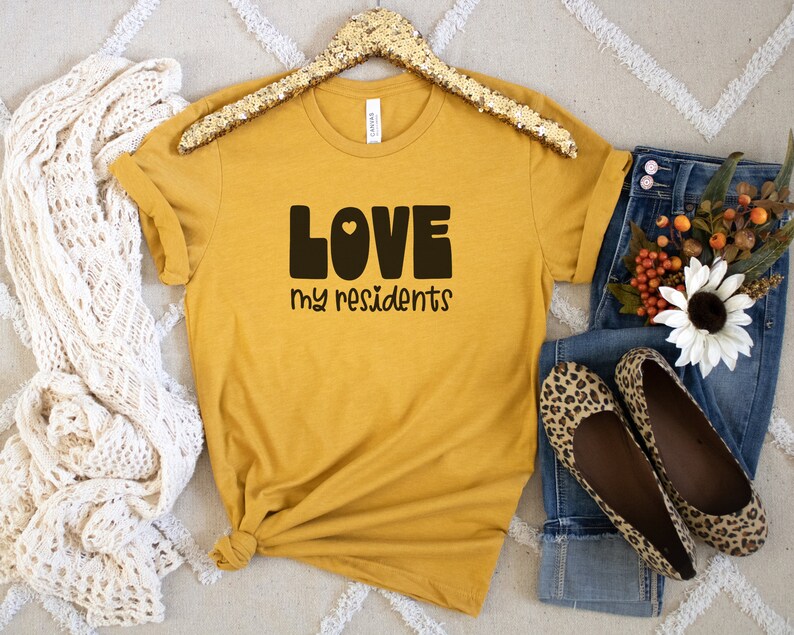 K&ouml;nnte beinhalten: Ein senfgelbes T-Shirt mit dem Text "LOVE my residents" in schwarzen Blockbuchstaben mit einem kleinen Herzen im "O".