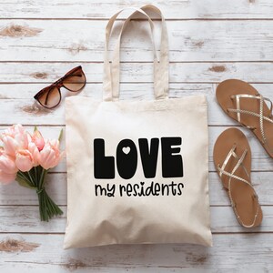 K&ouml;nnte beinhalten: Eine wei&szlig;e Canvas-Tragetasche mit schwarzem Text, der "LOVE my residents" lautet, mit einem kleinen wei&szlig;en Herzen in der Mitte des Wortes "LOVE".