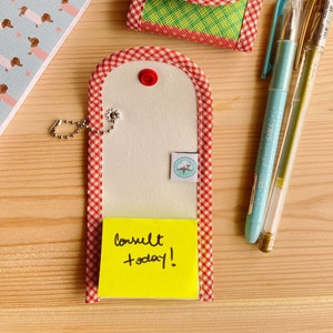 May include: Two small fabric pouches with red and white gingham trim and keychains. One pouch is green, red, and blue with a red button. The other pouch is white with a yellow sticky note that says "consult today!"