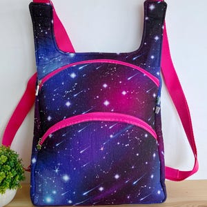 以下が含まれることがあります： ピンクとブルーの銀河柄のバックパック。ジッパー付きポケットが2つと調節可能なストラップが付いています。
