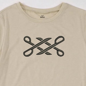 May include: A beige t-shirt featuring a dark green embroidered design. The design is an abstract pattern of intertwined shapes. The shirt has short sleeves and a crew neck. The fabric appears to be a soft cotton blend.