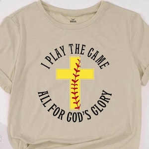 May include: A beige t-shirt with a black and red graphic of a baseball cross with the text "I Play The Game All For God's Glory".