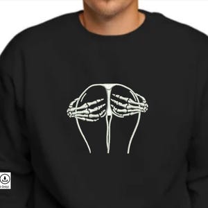 Könnte beinhalten: Ein schwarzes Sweatshirt mit einem weißen gestickten Design von Skeletthänden, die ein Paar Gesäß bedecken.