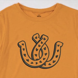 May include: A yellow t-shirt with a black embroidered design of two intertwined horseshoes with hearts on them.