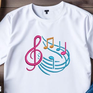 Könnte beinhalten: Weißes T-Shirt mit einem gestickten Design aus einem Violinschlüssel und Noten in Rosa, Blau und Gelb.