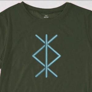 May include: Olive green t-shirt featuring a light blue geometric design on the front. The design is a stylized symbol. The shirt has short sleeves and a crew neck. The brand name is visible on the neckline.
