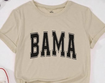 May include: A beige t-shirt with the word "BAMA" printed in black block letters.