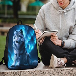 May include: A black backpack featuring a vibrant graphic print of a grey wolf sitting against a backdrop of glowing blue light streaks. The backpack has a rounded top, a main zippered compartment, and black side mesh pockets for storage.