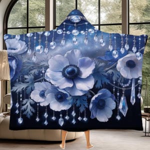 May include: A hooded blanket featuring a dark blue background with large, light blue anemone flowers and hanging crystal chandelier accents. The design includes a pointed hood and a starry night sky pattern integrated into the floral arrangement.