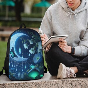 May include: A black backpack featuring a vibrant graphic print of a glowing crescent moon, a dark butterfly, hanging crystal charms, white flowers, and luminous green mushrooms against a deep blue, ethereal night sky background.