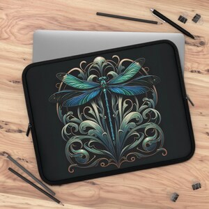 May include: Black laptop sleeve featuring a detailed illustration of a dragonfly with blue and green wings, set against an ornate, swirling, teal and gold background. The sleeve has a black zipper and trim.