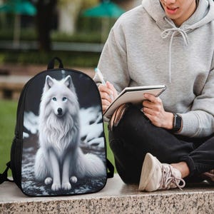May include: A black backpack featuring a high-resolution graphic print of a white wolf with piercing blue eyes sitting in a snowy landscape. The backpack has a rounded top, black side mesh pockets, and adjustable shoulder straps for carrying.