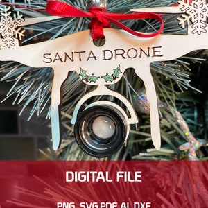 May include: A wooden Christmas ornament shaped like a drone with the words "Santa Drone" written on it. The drone has a red ribbon and a small camera lens.