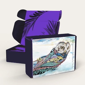 May include: A purple box with a matching lid, featuring a palm leaf design. The box contains a deck of cards with an owl illustration and the text "Transparent Owl Oracle Deck". The owl has colorful patterns.