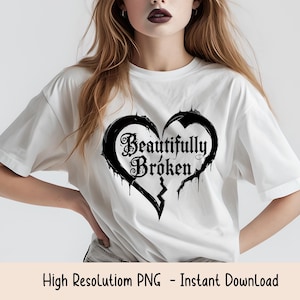 May include: White t-shirt featuring a black heart design with the words "Beautifully Broken" in gothic lettering. The heart is split down the middle. The shirt is a casual style.