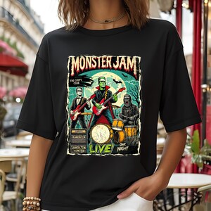 May include: Black t-shirt featuring a colorful graphic of a monster band playing instruments. The design includes the text "MONSTER JAM" and "LIVE" with other text. The band consists of Frankenstein, a werewolf, and a musician.