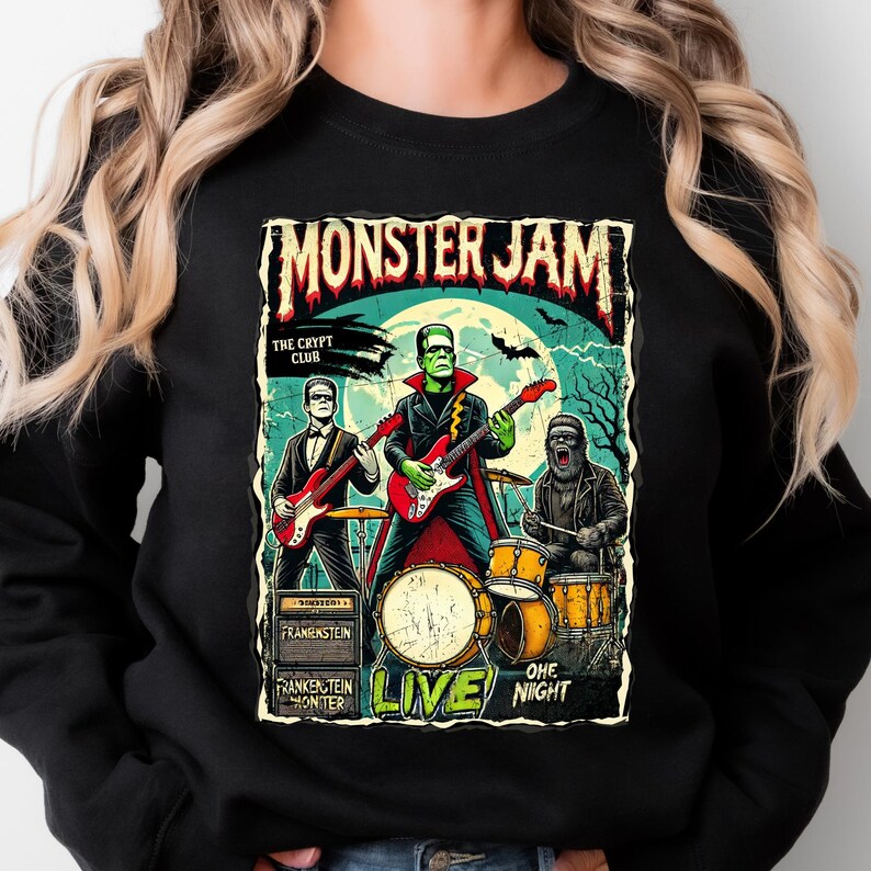 May include: Black sweatshirt featuring a Monster Jam concert poster design. The graphic depicts a band of monsters playing instruments, with Frankenstein on guitar. The text reads "Monster Jam", "The Crypt Club", and "Live One Night".