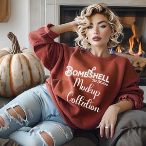 May include: A rust-colored sweatshirt with the text "Bombshell Tee Studio Mockup Collection" in white. The sweatshirt is paired with ripped blue jeans. A large pumpkin with a tan and white striped pattern is visible.