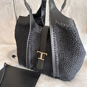 May include: Black woven tote bag with leather accents and a matching small pouch. The tote features a leather strap with a gold-tone buckle. The bag has two handles and a woven texture. The pouch has a braided strap.