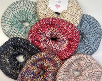 May include: Set of six knitted hair scrunchies in various colors and patterns, including teal, red, black, pink, and multi-colored. The scrunchies are handmade with love, as indicated by the tag.