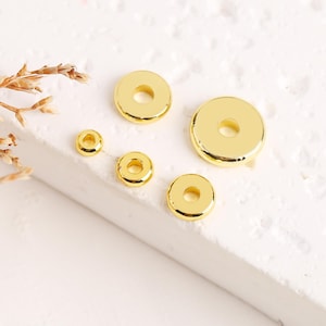 May include: Five gold-colored metal spacer beads of varying sizes. The beads are round with a hole in the center.