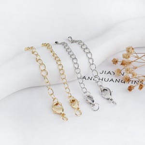 May include: Four metal chain extenders in gold and silver. Each extender has a series of oval links and a lobster clasp closure. The extenders are designed to add length to necklaces or bracelets.