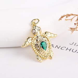 May include: A gold-tone turtle pendant with a green gemstone and clear rhinestones. The pendant is detailed with a textured shell and a loop for attaching a chain.