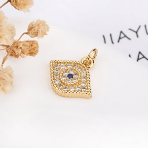 May include: Gold evil eye charm with a blue center and clear rhinestones. The charm is in the shape of a diamond and has a loop at the top for attaching to a necklace or bracelet.
