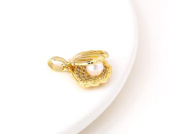 May include: A gold-colored pendant in the shape of an open seashell, with a pearl nestled inside. The seashell is detailed with textured ridges and small, sparkling accents around the pearl. The pendant has a loop for a chain.