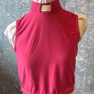 May include: A sleeveless, magenta-colored top with a high, open-back collar. The top is made of a soft fabric and has a gathered hemline. The garment is displayed on a mannequin.