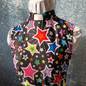 May include: A black top with a vibrant star pattern in various colors, including pink, orange, yellow, green, blue, and purple. The top has a high collar and is paired with a white garment underneath. The overall style is eye-catching and playful.