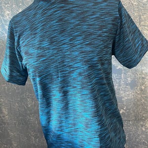 Könnte beinhalten: Ein kurzärmeliges Hemd mit hohem Kragen und weißem Lascheneinsatz. Das Hemd hat ein blau-schwarzes Muster und eine strukturierte Optik. Der Stoff ist wahrscheinlich atmungsaktiv.