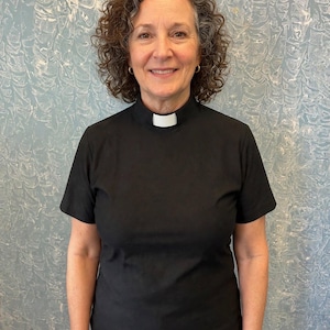 May include: A black short-sleeved shirt featuring a high mock neck collar with a white rectangular clerical tab insert at the center front. The garment is constructed from a solid black fabric and is designed with a standard fit, short sleeves, and a clean, finished neckline that accommodates the removable white clerical tab.