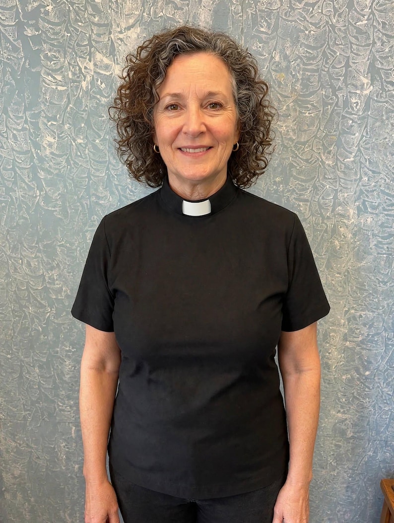 May include: A black short-sleeved shirt featuring a high mock neck collar with a white rectangular clerical tab insert at the center front. The garment is constructed from a solid black fabric and is designed with a standard fit, short sleeves, and a clean, finished neckline that accommodates the removable white clerical tab.