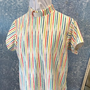 May include: A short-sleeved shirt with a high mock neck collar, featuring a vertical striped pattern in shades of red, lime green, and teal blue on a white background. The garment is displayed on a mannequin, showcasing a straight hemline.