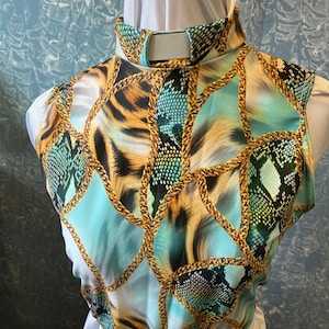 May include: A sleeveless top with a high collar. The top features a print with gold chain links, animal print, and a teal and black snakeskin pattern. The top is displayed on a white mannequin.