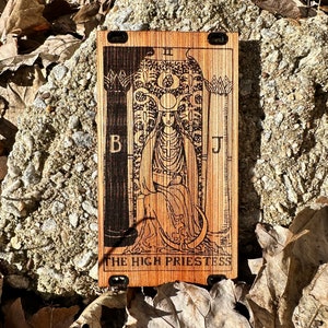 May include: A wooden tarot card with a black and white image of the High Priestess. The card is labeled with the Roman numeral II and the text "THE HIGH PRIESTESS".