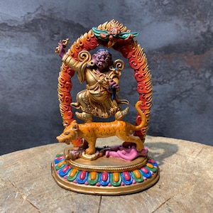 May include: A detailed figurine of a deity with a purple face and gold clothing, standing on a tiger. The figure is framed by a red and orange arch with a dragon at the top. The base is gold with colorful accents.