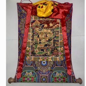 May include: A colorful Tibetan prayer scroll with a red border and intricate patterns. The scroll depicts a scene with animals and trees, and is mounted on wooden dowels.
