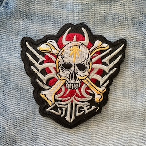 May include: A black and white embroidered patch with a skull and crossbones design. The skull is white with black eyes and a red and yellow background. The text "JICE" is embroidered in white on a black background.