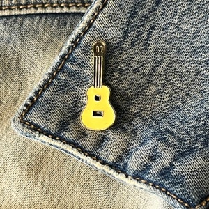 May include: A yellow metal guitar pin on a blue denim background.