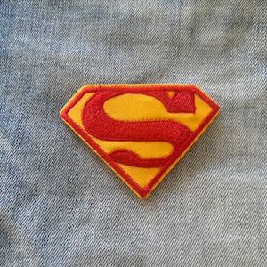 May include: A red and yellow embroidered Superman logo patch. The patch is in the shape of a diamond and has a red 'S' on a yellow background.