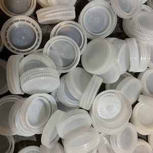 May include: A pile of white plastic bottle caps. The caps are all different sizes and shapes, but they are all made of the same material.