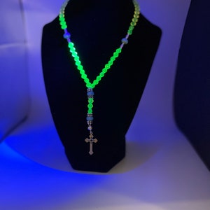 May include: A green glass beaded necklace with a silver cross pendant. The beads are glowing under a black light.