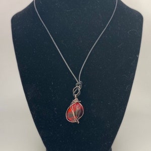 May include: A red gemstone pendant necklace with a silver wire wrap. The necklace is on a black cord.