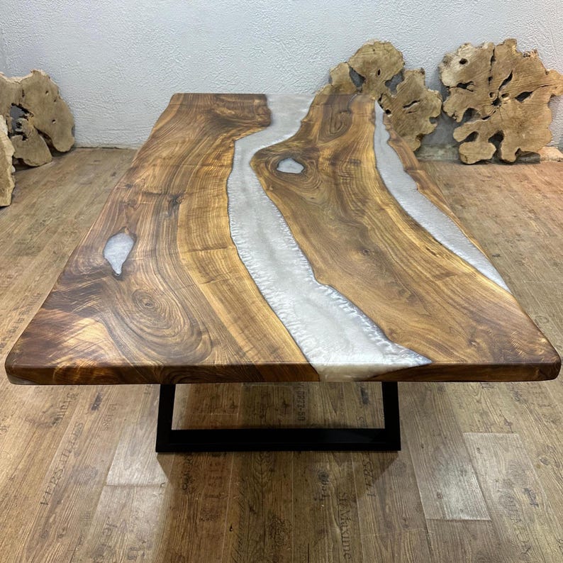 以下が含まれることがあります： 中央に銀色の樹脂の川が流れる、手作りの木製テーブル。 テーブルは濃い茶色の仕上げで、黒い金属製のベースの上にあります。 木目は見えます。