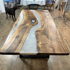 以下が含まれることがあります： 明るい灰色の樹脂川のデザインが施された、大きな長方形の木製テーブル。 テーブルは濃い茶色の木材でできており、黒い金属製のベースの上にあります。 テーブルの長さは約244cm、幅は約102cmです。