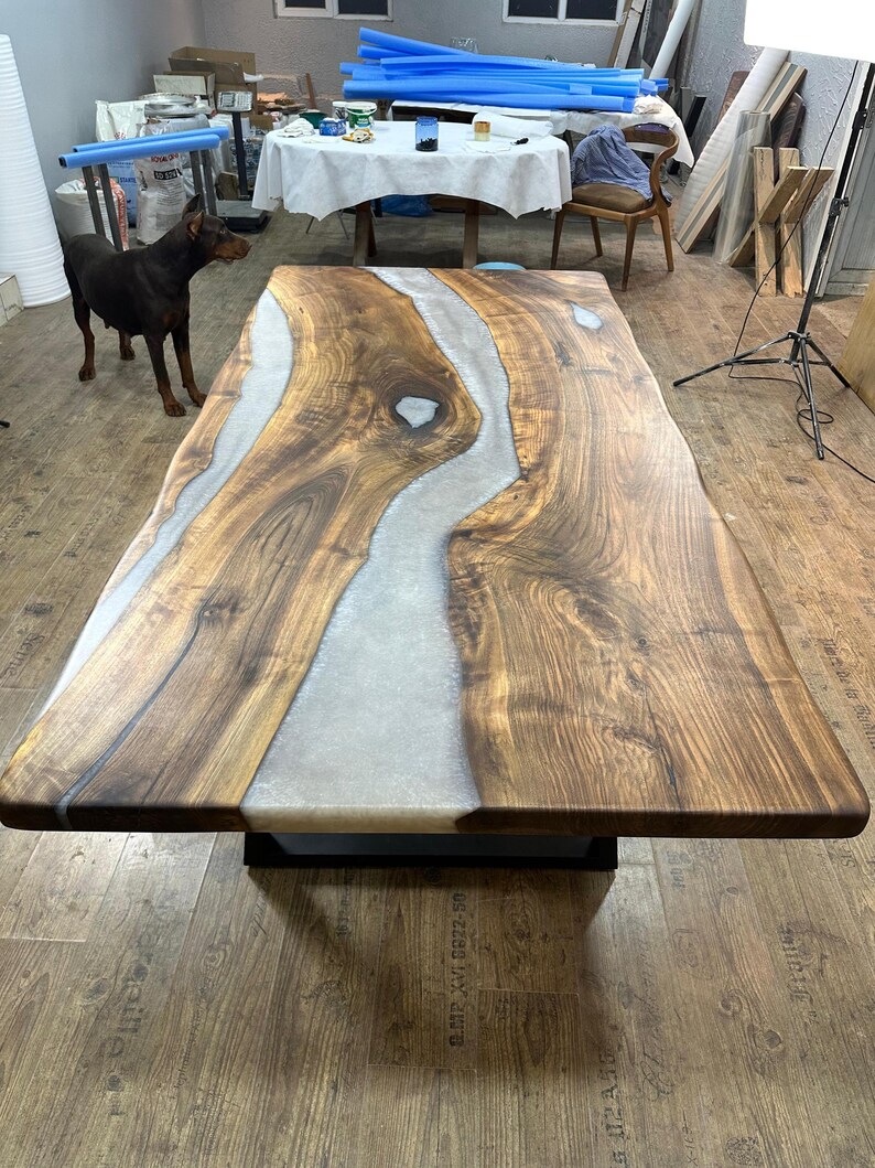 以下が含まれることがあります： 明るい灰色の樹脂川のデザインが施された、大きな長方形の木製テーブル。 テーブルは濃い茶色の木材でできており、黒い金属製のベースの上にあります。 テーブルの長さは約244cm、幅は約102cmです。