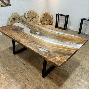 以下が含まれることがあります： 生きたエッジと中央を流れる透明なエポキシ樹脂の川がある、大きな長方形の木製テーブル。 テーブルは濃い茶色の仕上げで、黒い金属製の脚の上にあります。 テーブルの長さは約183cmです。