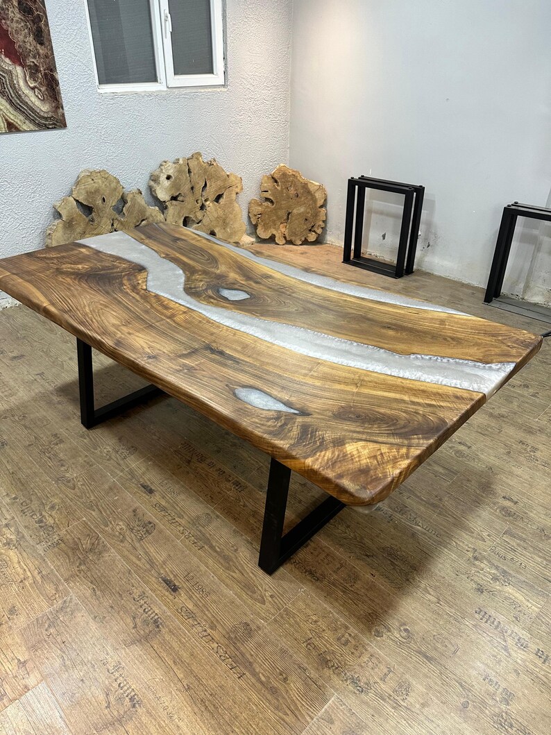 以下が含まれることがあります： 生きたエッジと中央を流れる透明なエポキシ樹脂の川がある、大きな長方形の木製テーブル。 テーブルは濃い茶色の仕上げで、黒い金属製の脚の上にあります。 テーブルの長さは約183cmです。